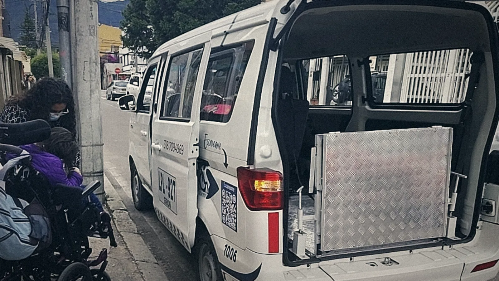 Van GO con la puerta trasera abierta y la plataforma lista; una paciente en silla de ruedas espera junto a su cuidadora